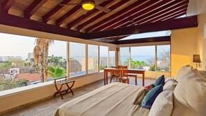 A bedroom with a large window, a bed, a table, and a ceiling fan.