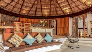 A modern interior with a thatched roof, a stone wall, a wooden kitchen, and a seating area with cushions.