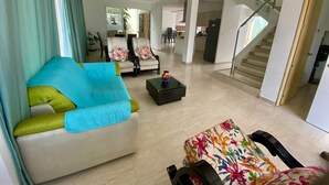 Un salon spacieux, aménagé avec un canapé, des fauteuils et une table basse. Un escalier mène à un autre niveau.
