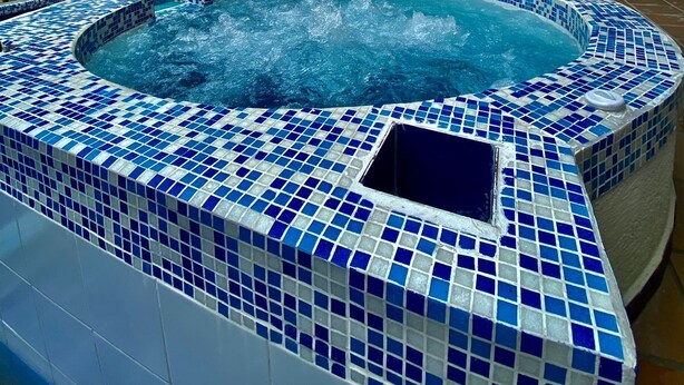 Une piscine intérieure moderne, avec des carreaux de mosaïque bleus, un mur en briques et un bâtiment à plusieurs niveaux en arrière-plan.
