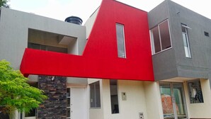 Une maison moderne dotée d’une façade unique aux couleurs rouge et grise, d’un mur d’accent en pierre et d’un petit jardin à l’avant, avec des marches menant à l’entrée.