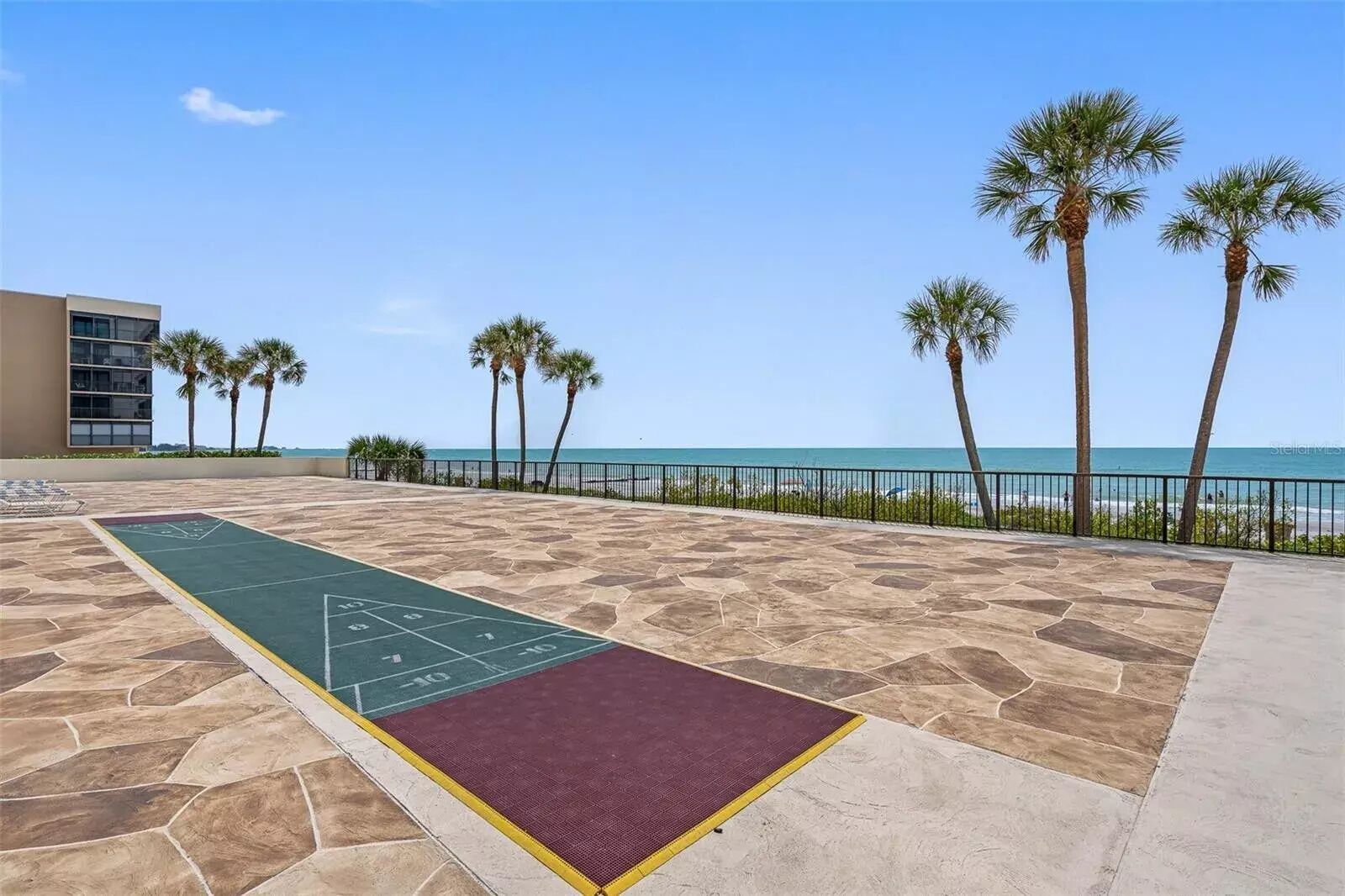 A shuffleboard court with a view of the beach and palm trees.