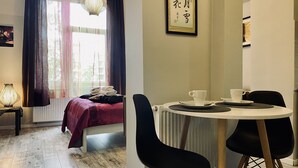A room with a bed, a table with chairs, a window with curtains, and a wall-mounted picture frame. - Apartment next to charming Vistula Boulevards, Pekin (Kraków)