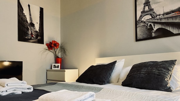 Ein Hotelzimmer mit Bett, Kissen, Nachttisch, Fernseher und Bildern an der Wand.