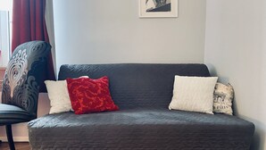 Ein dunkelgraues gestepptes Sofa mit drei Kissen, ein gemustertes Sessel und ein gerahmtes Bild an der Wand.