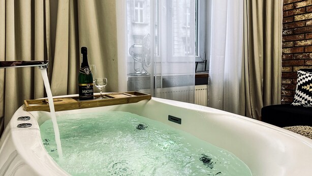 A bathtub with running water, a bottle of champagne, and a glass on a tray. - Apartment Premium Jacuzzi for couples, Old Town I, Starowiślna (Kraków)