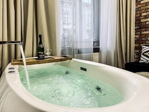 A bathtub with running water, a bottle of champagne, and a glass on a tray. - Apartment Premium Jacuzzi for couples, Old Town I, Starowiślna (Kraków)