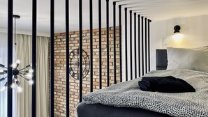 A modern bedroom with a brick wall, a large clock, a bed with patterned bedding, and a ceiling light fixture. - Apartment Premium Jacuzzi for couples, Old Town I, Starowiślna (Kraków)