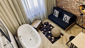 A modern bathroom with a freestanding bathtub, a black sofa with patterned cushions, and a wooden side table. - Apartment Premium Jacuzzi for couples, Old Town I, Starowiślna (Kraków)