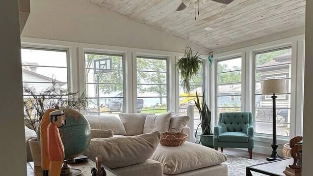 A spacious living room with a high ceiling, large windows, a ceiling fan, and a cozy seating area with a sofa and armchairs. - The CREW House at Bass Lake, IN (Bass Lake)
