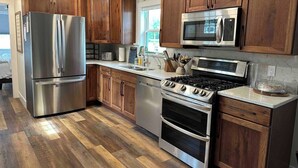 A modern kitchen with stainless steel appliances, wooden cabinets, and a herringbone-patterned floor. - The CREW House at Bass Lake, IN (Bass Lake)