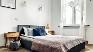 Une chambre à coucher moderne avec un lit, des tables de chevet, une carte accrochée au mur et une fenêtre ornée de rideaux légers.