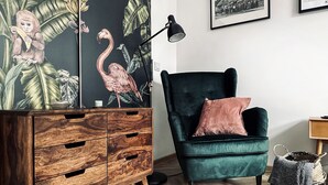 Une pièce comprenant un fauteuil en velours vert foncé, une commode en bois avec de nombreux tiroirs, un lampadaire noir et un panier en osier posé sur le sol.