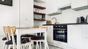 Une cuisine moderne avec des meubles blancs, un four noir et une table à manger en bois, accompagnée de chaises.