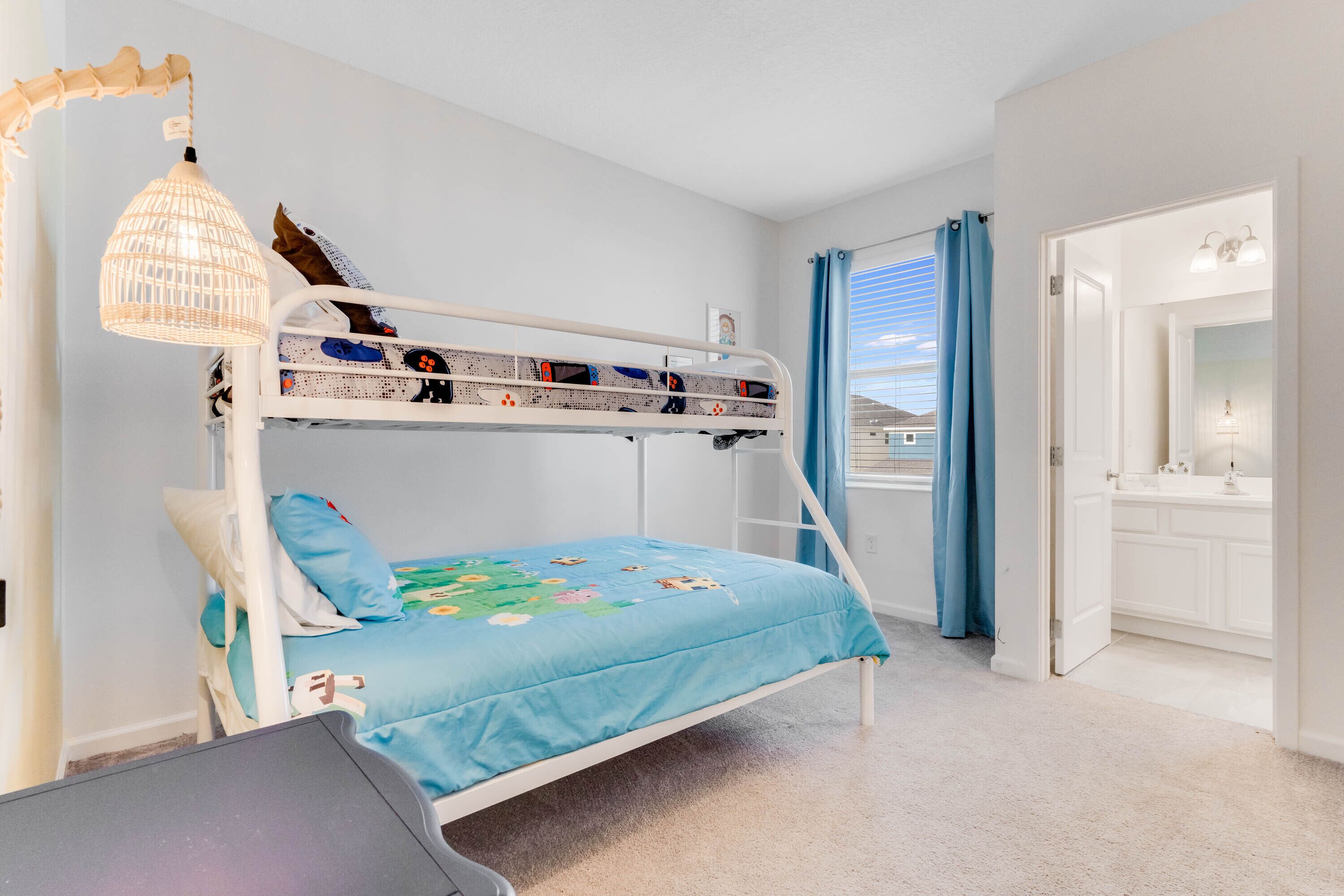 A bunk bed with a blue bedspread, a hanging lamp, and a view of the outdoors through a window with blue curtains.