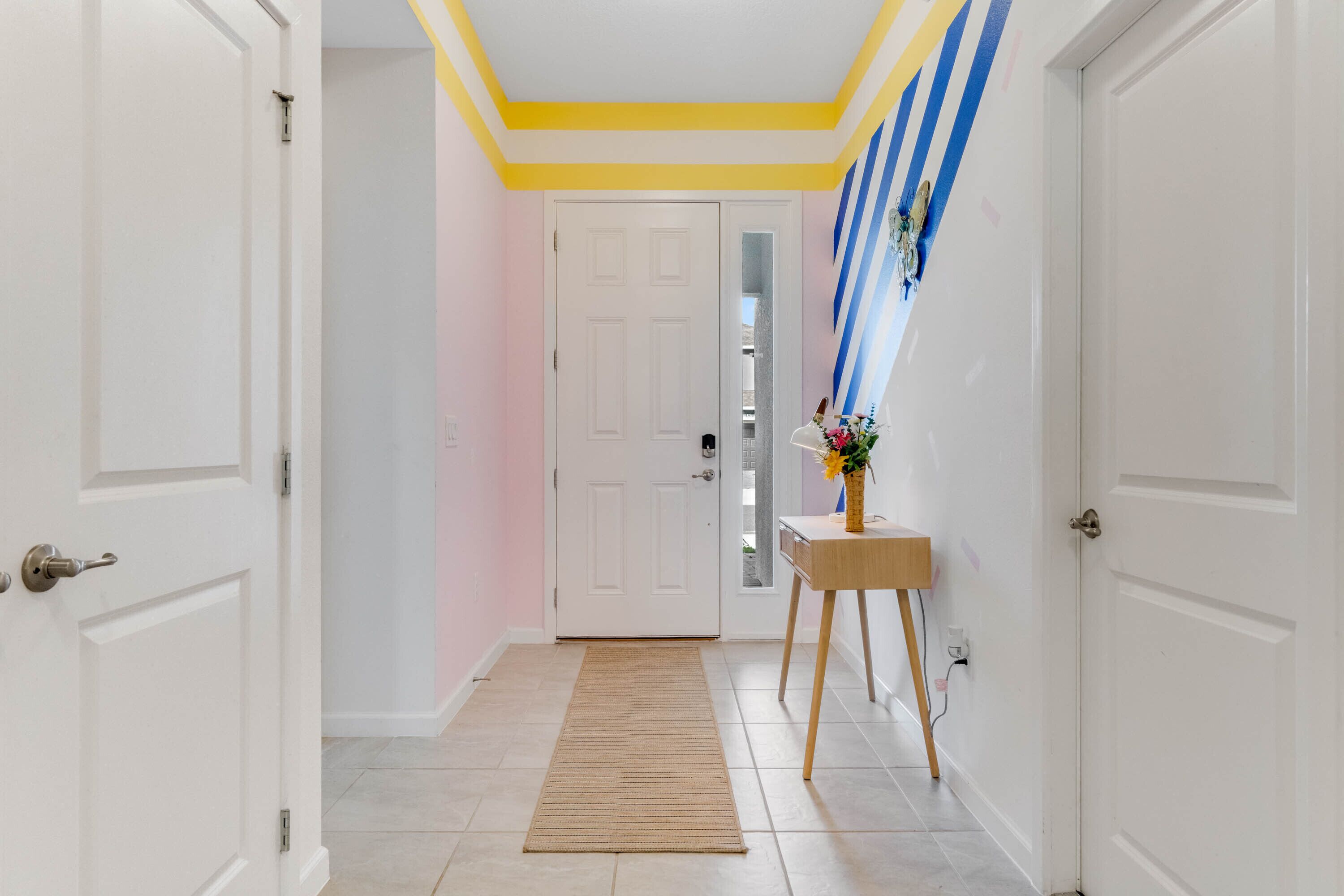 A hallway with white doors, a wooden side table with a vase, and a striped wall decoration.