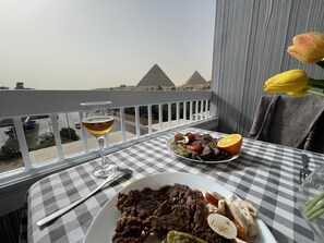 Una mesa en el balcón con mantel a cuadros, un plato de comida, una copa de vino y vistas a las pirámides.