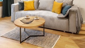Un salon moderne avec un canapé gris, des coussins jaunes et bleus, une table basse ronde en bois et un lampadaire.