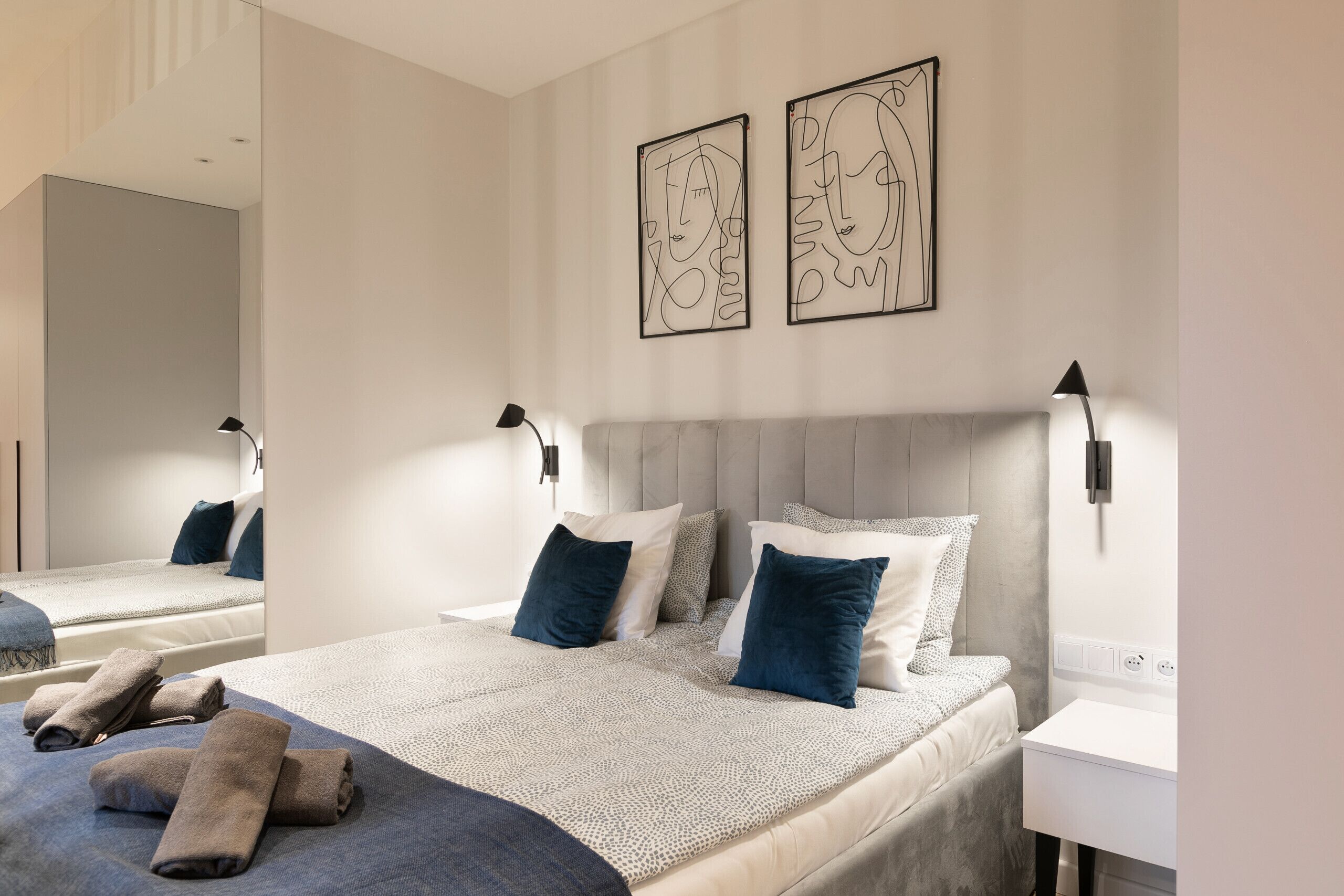 Ett hotellrum med en stor säng, två sängbord, en spegel och konstverk på väggen.