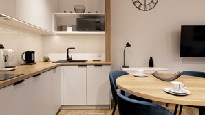 Une cuisine moderne avec des meubles blancs, un four à micro-ondes et une machine à café. On y trouve également un coin repas avec une table ronde et des chaises bleues.