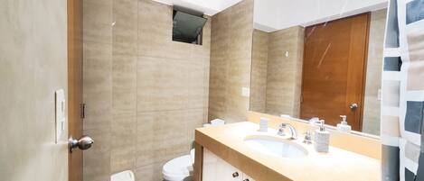 A modern bathroom with a beige tiled wall, a white toilet, a sink with a mirror, and a shower curtain.