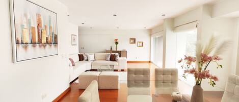 A modern living room with a sofa, armchairs, a coffee table, and a large painting on the wall.