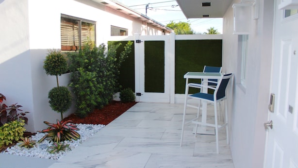 En moderne patio med et hvidt bord og stole, omgivet af veltrimmede hække og forskellige planter.