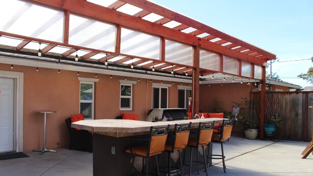 Un patio al aire libre con una zona de bar, asientos y una pérgola.