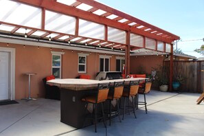 Een terras buiten met een bar, zitplaatsen en een pergola.