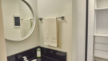 A bathroom with a black countertop, a mirror, a towel rack with a towel, and a bottle of hand soap.