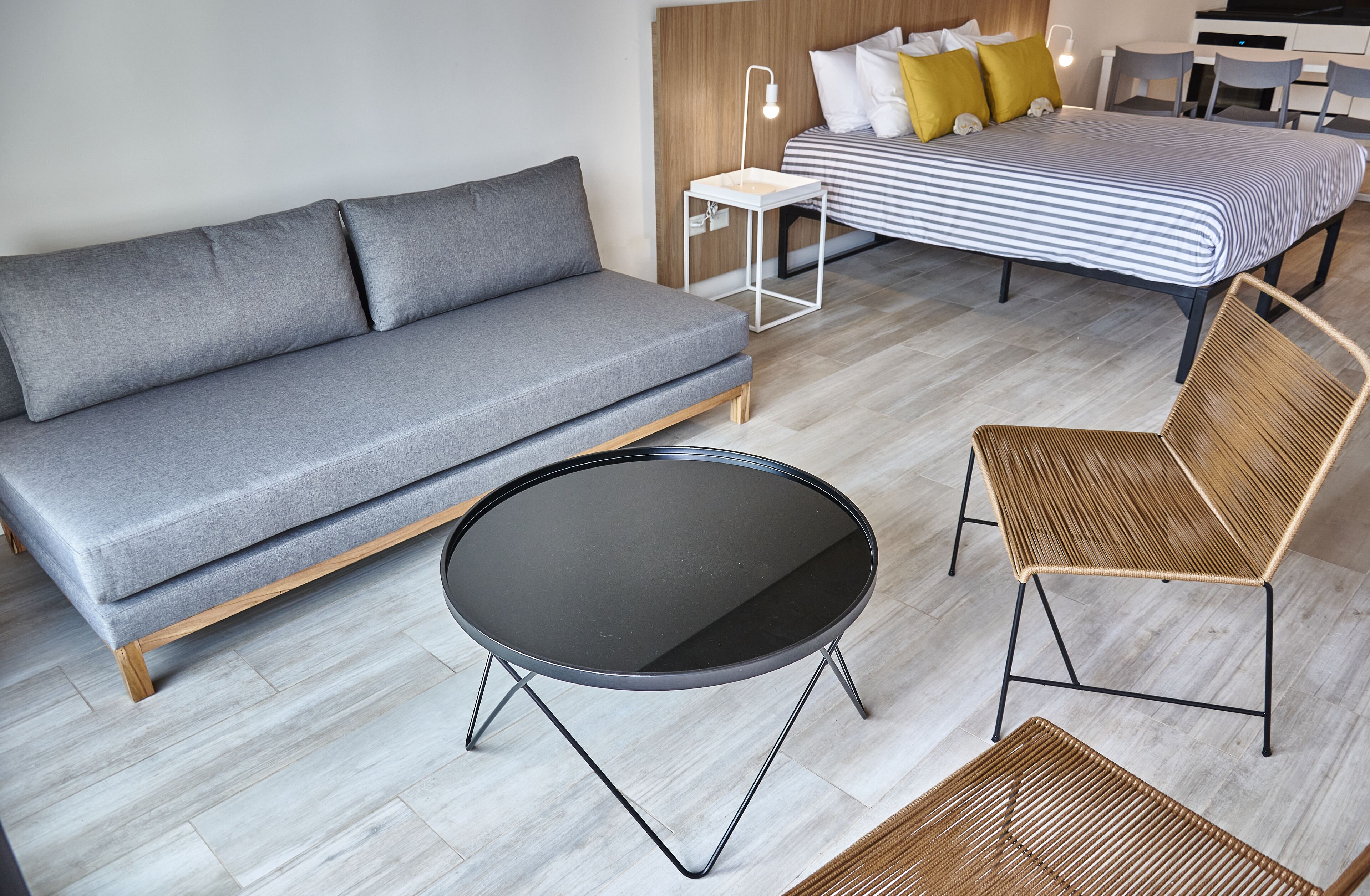 A modern room with a grey sofa, a round black table, and a wicker chair.