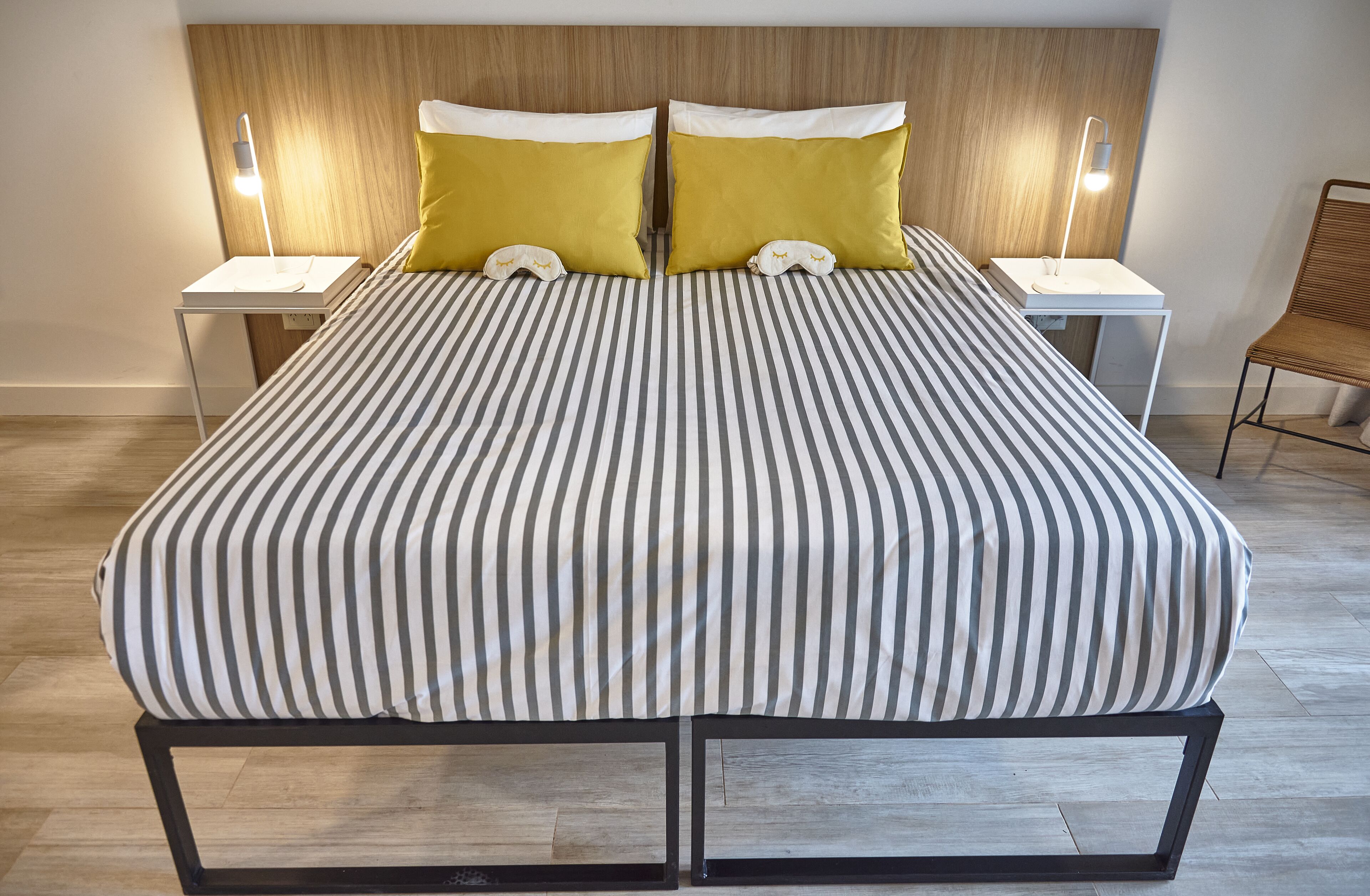 Una cama doble con ropa de cama a rayas, dos mesitas de noche con lámparas y un cabecero de madera.