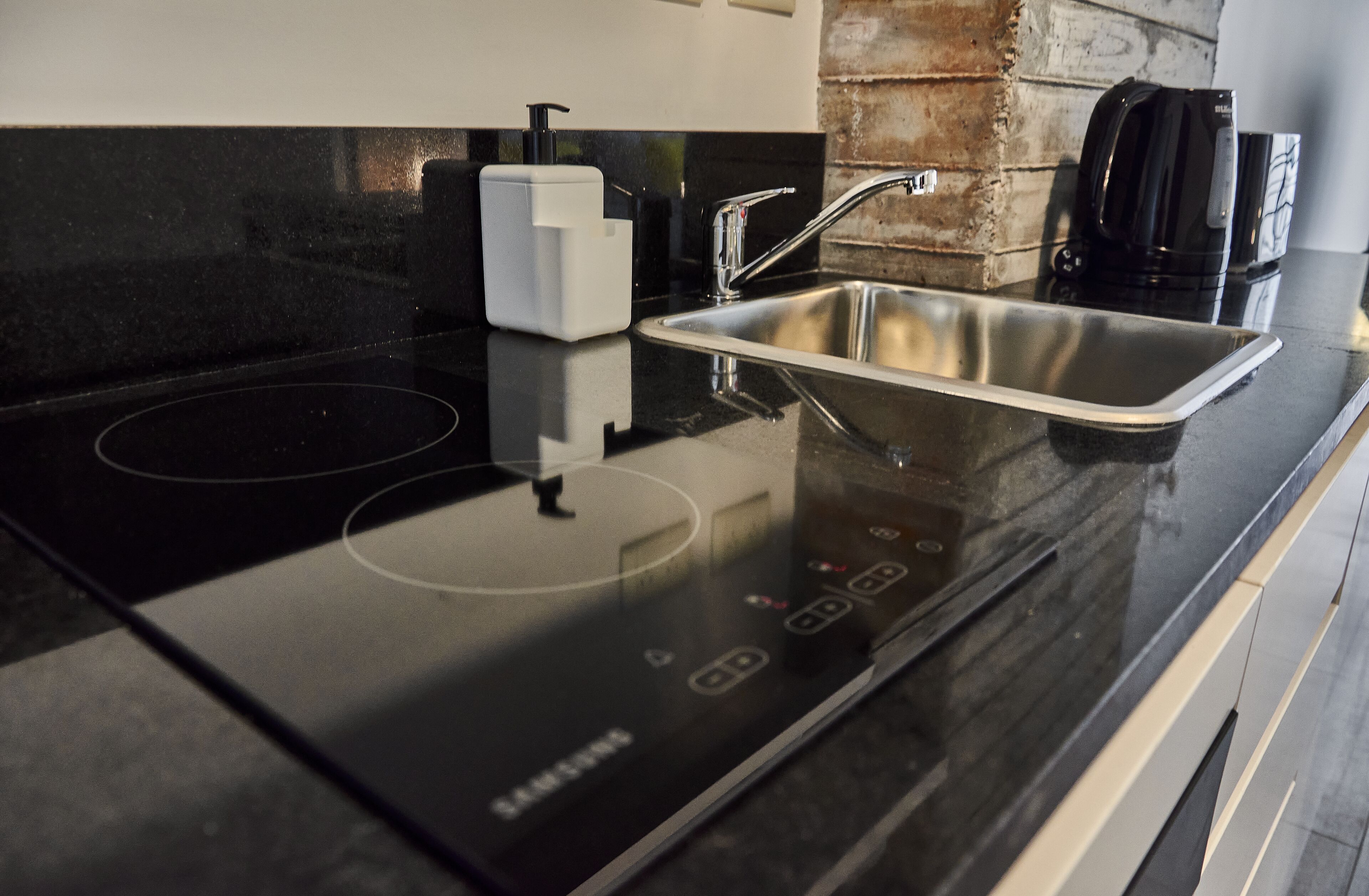 A modern kitchen with a black induction cooktop, stainless steel sink, and a coffee maker.