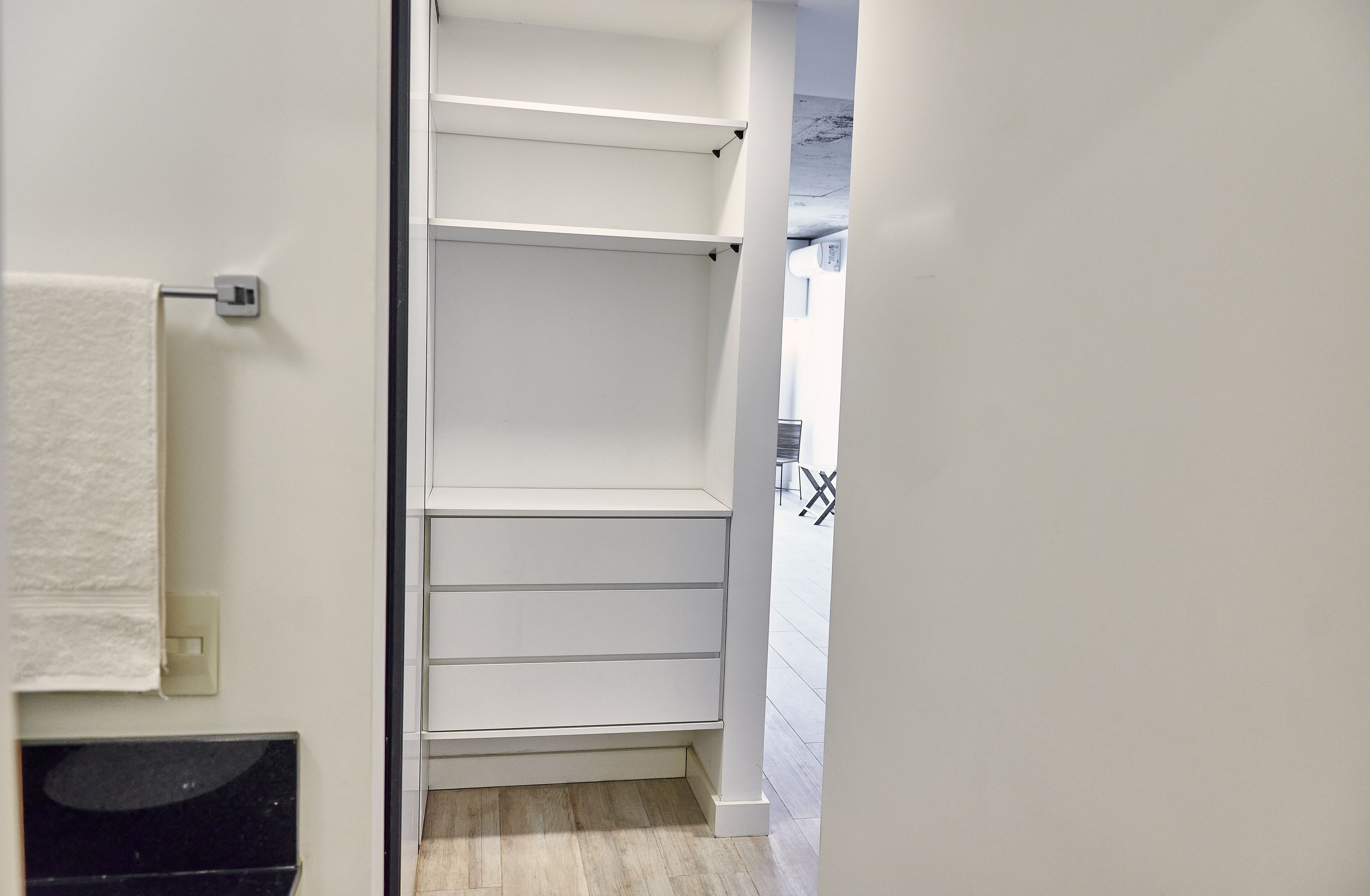 Una cabina armadio con scaffali aperti e un elettrodomestico nero sottostante.