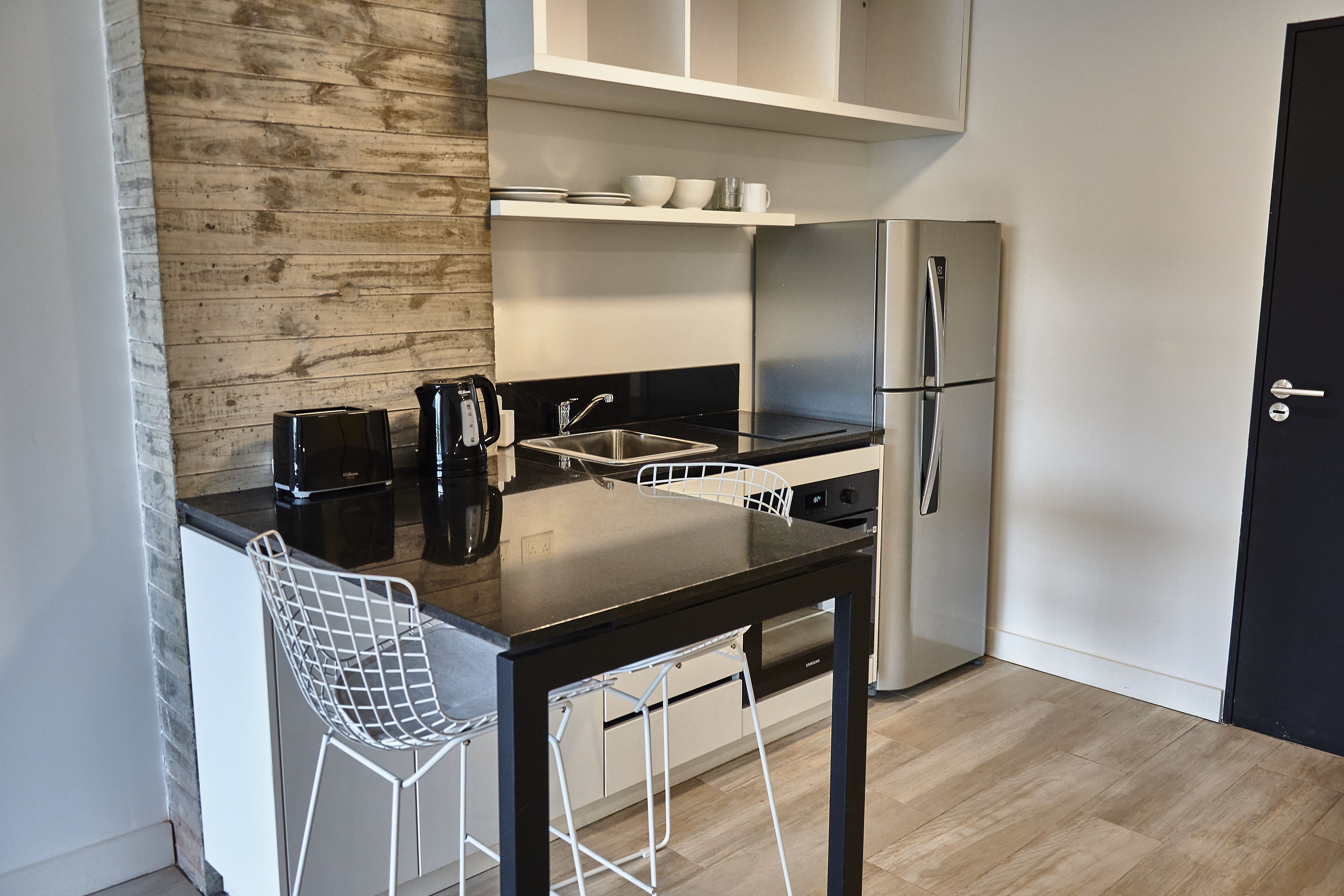 Une cuisine moderne avec un plan de travail noir, des appareils en acier inoxydable, des tabourets de bar blancs et des éléments décoratifs en bois.