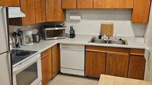 Una cocina compacta con armarios de madera, un microondas, un lavavajillas y un fregadero.