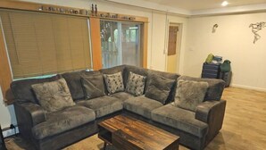 Un salón con un sofá modular, una mesa de centro de madera y un ventanal con persianas.
