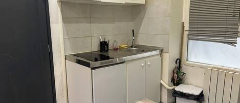 A compact kitchen with a black door, white cabinets, a stainless steel countertop, a sink, and a window with blinds.