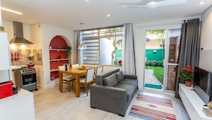 Un salon moderne avec un canapé gris, un coin repas avec une table en bois et une cuisine équipée d’une cuisinière et d’un four.