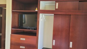 Ein Holzschrank mit mehreren Fächern, darunter ein Ablagebereich mit einem Fernseher und einer Kleiderstange.