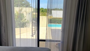 Ein Zimmer mit großem Fenster, Blick auf einen Swimmingpool und eine Betonmauer.
