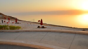 A beachside area with sun loungers and umbrellas, a concrete walkway, and a view of the sea at sunset. - PORTO & ALMIRA BEACH (Sweimeh)