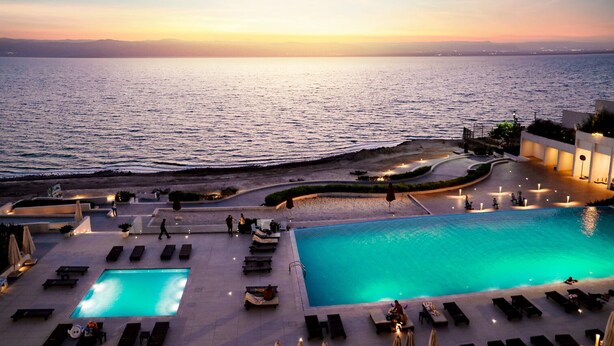 A resort pool area with multiple pools and sun loungers, a beach, and a view of the sea at sunset. - PORTO & ALMIRA BEACH (Sweimeh)
