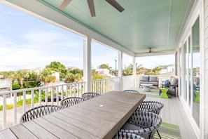 A covered outdoor patio with a wooden table and chairs, a seating area with cushions, and a view of the surrounding neighborhood. - Sweet Retreat by Tybee Vacation Rentals (Tybee Island)