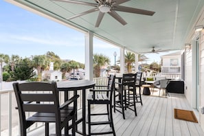 A covered outdoor patio with wooden furniture, ceiling fans, and a view of the surrounding neighborhood. - Sweet Retreat by Tybee Vacation Rentals (Tybee Island)