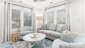 Een moderne woonkamer met een grijze bank, twee fauteuils, een salontafel en een lamp.