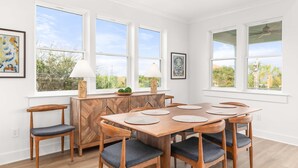 Een eetgedeelte met een houten tafel en stoelen, grote ramen en een decor kast.