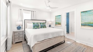 Een slaapkamer met een groot bed, twee nachtkastjes, een plafondventilator en kunstwerken aan de muur.