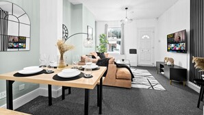En moderne stue med spiseplads, med en sofa, et sofabord og et fjernsyn monteret på væggen.