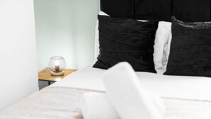 En pænt redt seng med hvidt og sort sengetøj, en rund bordlampe og et lille trænatbord.